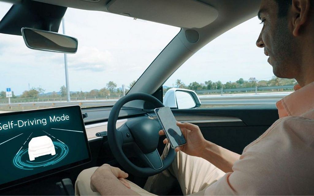 A man sitting in the driver's seat of a self-driving car, looking at his phone.