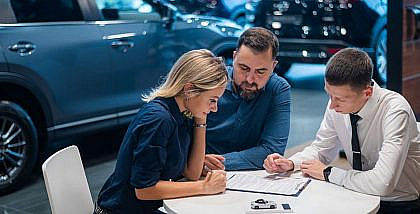 ثلاثة أشخاص في معرض سيارات يطلعون على عقد