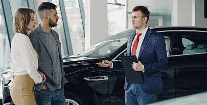 موظف مبيعات يسعاد عميلين في معرض سيارات