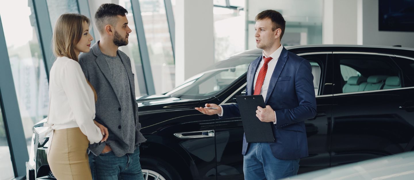 موظف مبيعات يسعاد عميلين في معرض سيارات
