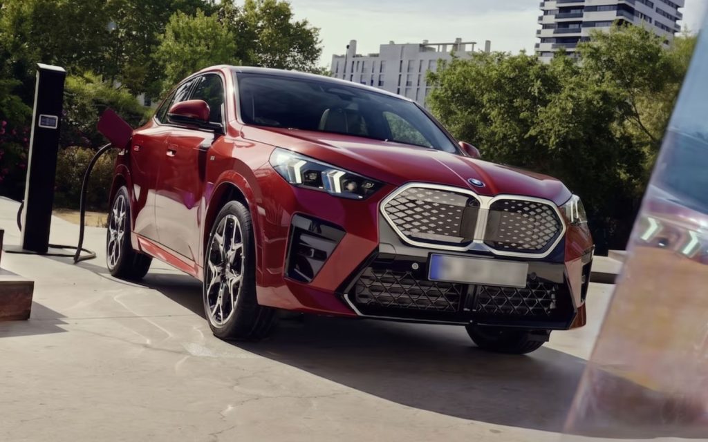 A metallic red BMW iX2 electric crossover is charging at a sleek black station