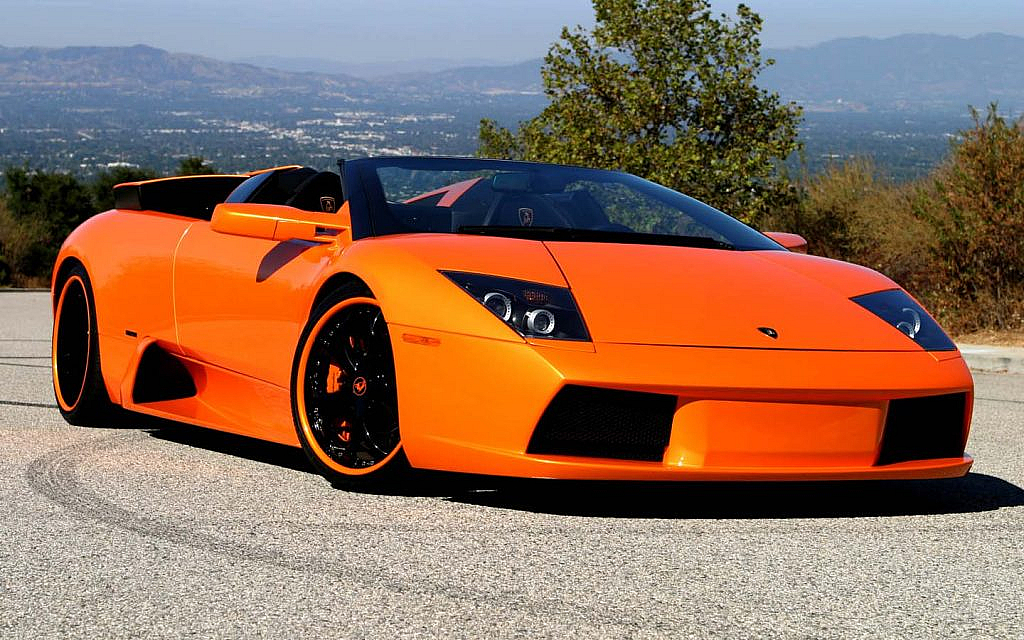 An orange Lamborghini Murciélago LP640 Roadster is parked on a scenic mountain road.