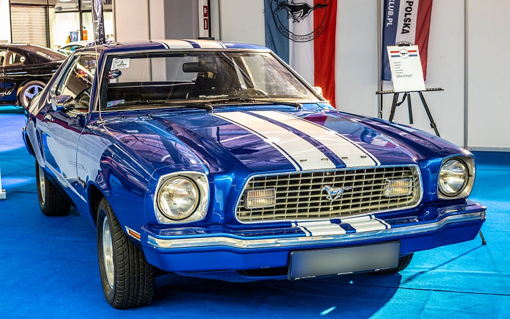 A blue second-generation Ford Mustang with white racing stripes on display at an indoor car show.