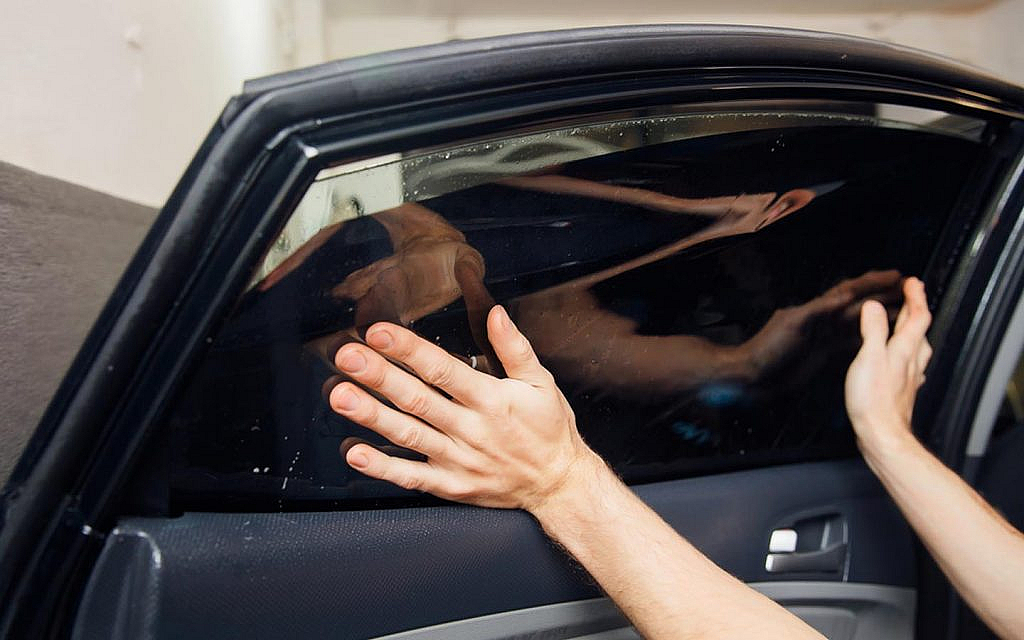 A person's hands carefully apply a dark window tint film.