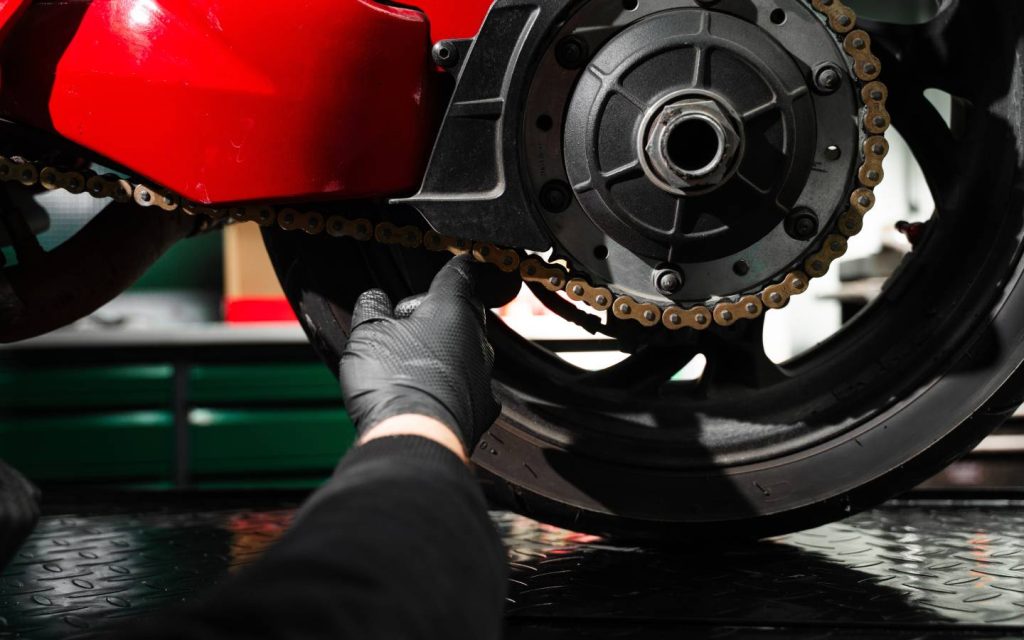 A hand inspecting the chain attached to a motorcycle sprocket
